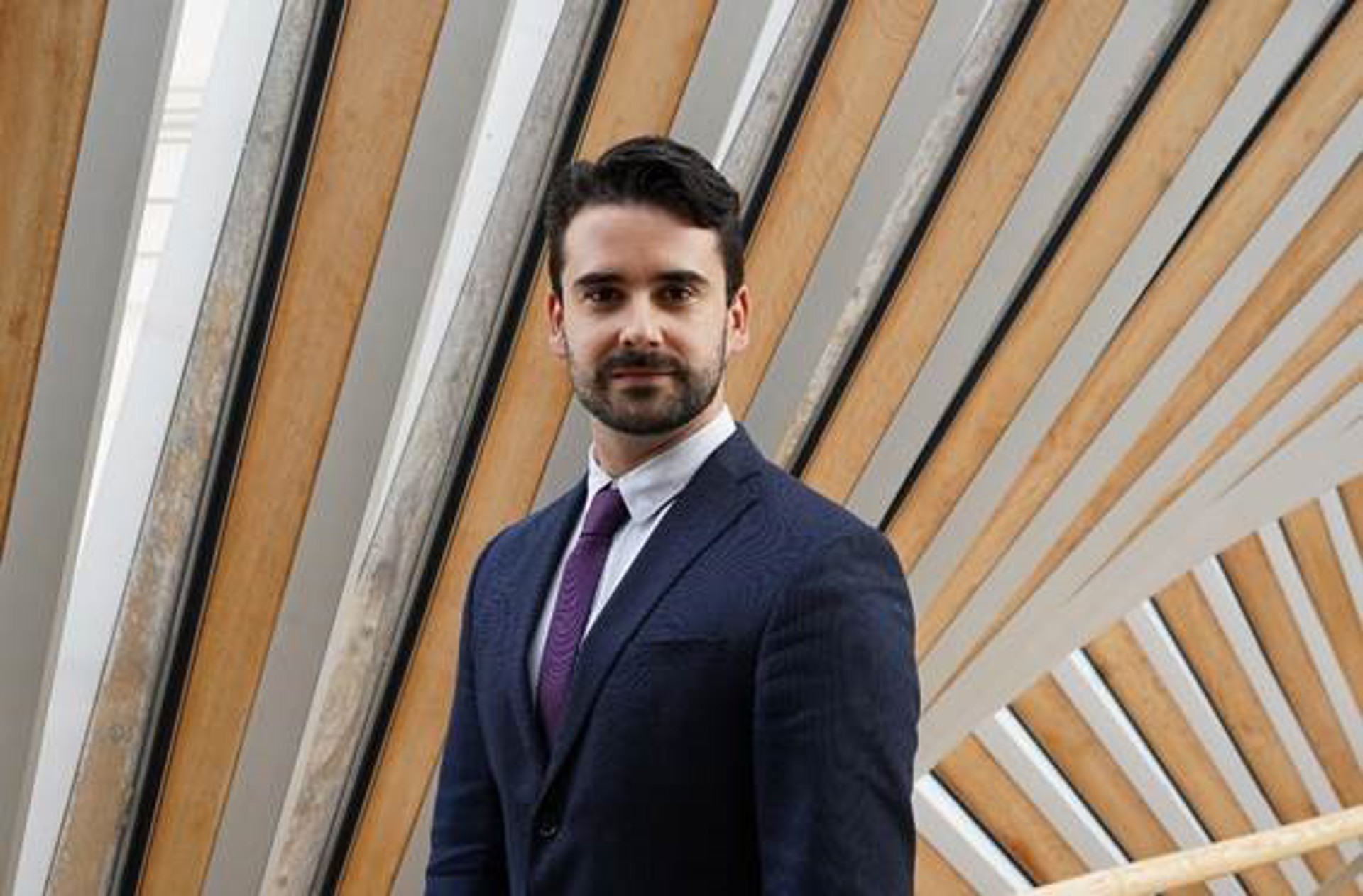 headshot of white male with dark hair and beard wearing blue suit and purple tie headshot of white male with dark hair and beard wearing blue suit and purple tie