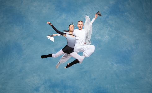 Two ballet dancers jumping in the air with a cloudy blue background