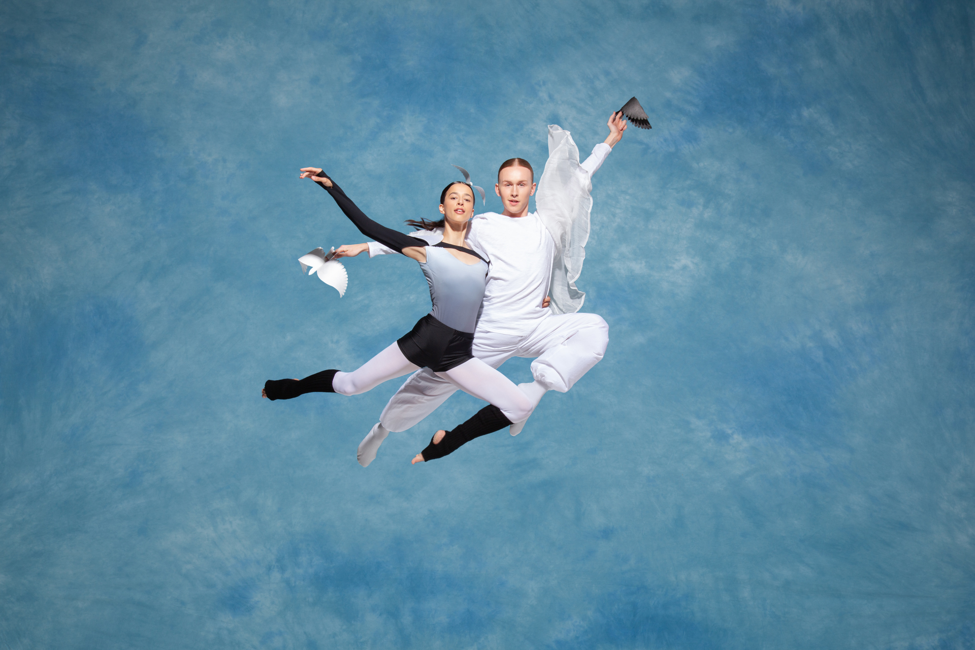 Two ballet dancers jumping in the air with a cloudy blue background Two ballet dancers jumping in the air with a cloudy blue background