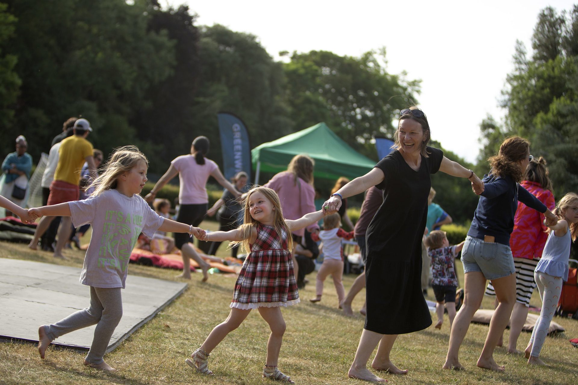 two young white female children holding hands with white female across the image in a field with trees behind two young white female children holding hands with white female across the image in a field with trees behind