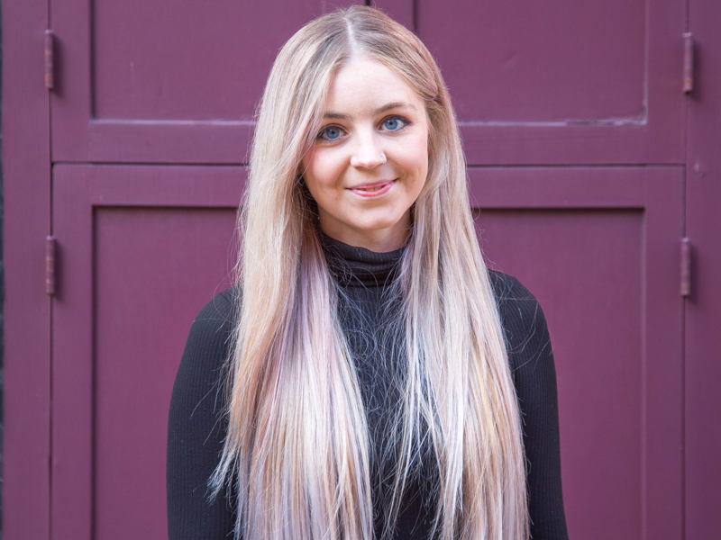 Headshot of Amelia Wilkinson. White female with long blonde hair smiling at the camera wearing long sleve black top in front red door Headshot of Amelia Wilkinson. White female with long blonde hair smiling at the camera wearing long sleve black top in front red door