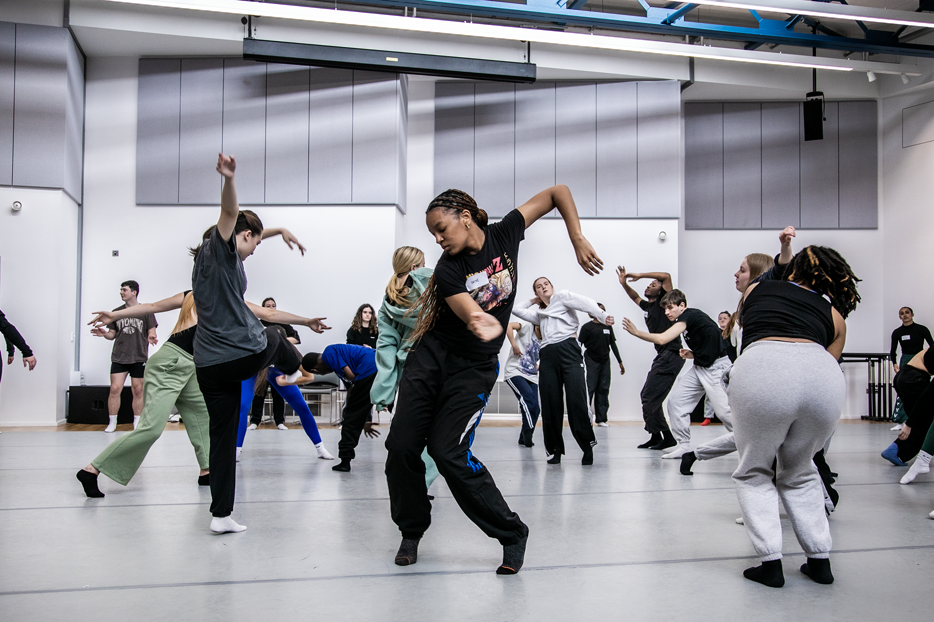 Young people dancing in a dance studio all interacting with each other. Main focus on global majority female dancer moving her arms to the right and swinging hair around. Young people dancing in a dance studio all interacting with each other. Main focus on global majority female dancer moving her arms to the right and swinging hair around.