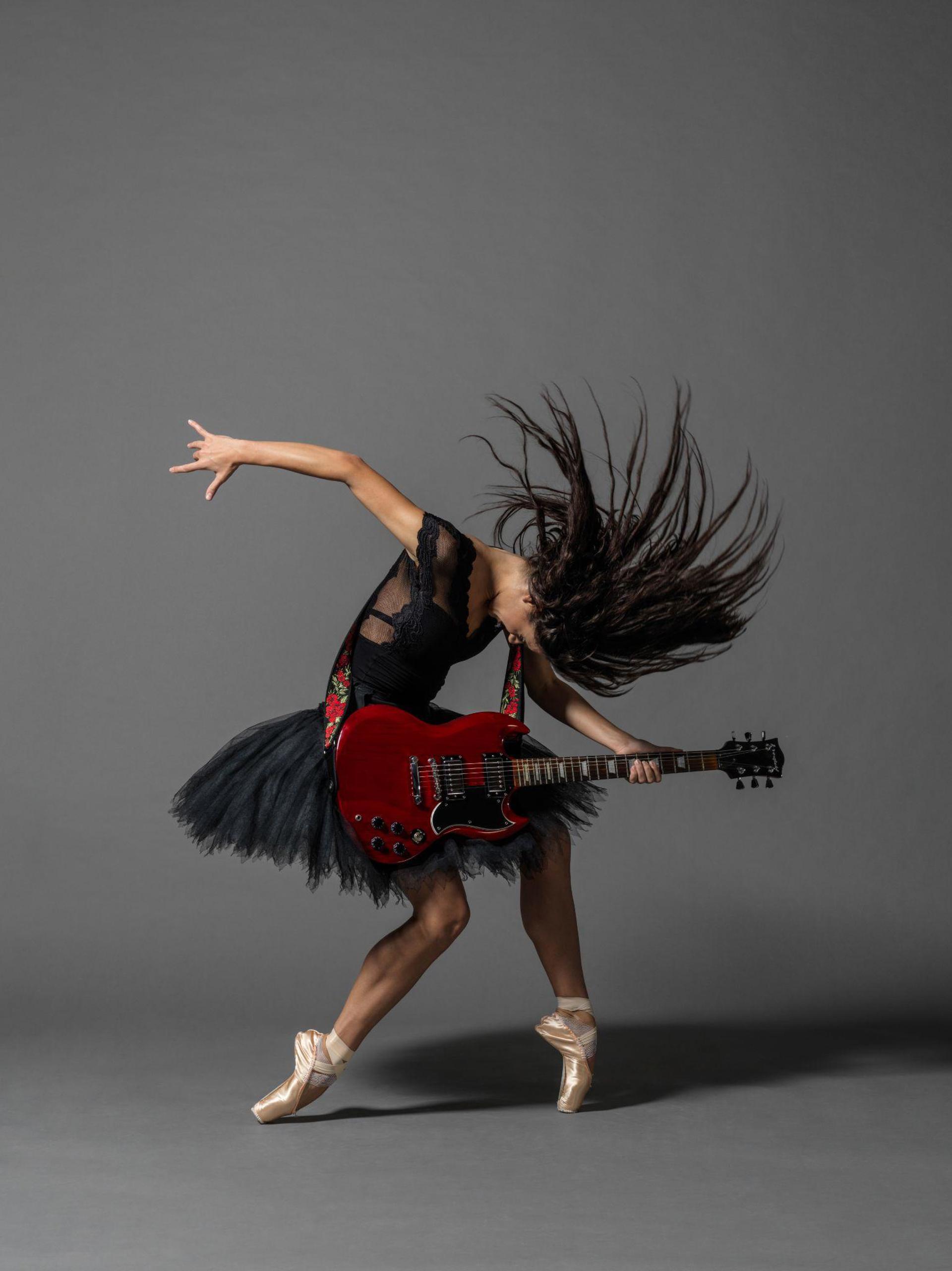 female dancer on point with bended knees, holding a guitar arching over it, with one hand flung behind and long brown hair flicked over the head female dancer on point with bended knees, holding a guitar arching over it, with one hand flung behind and long brown hair flicked over the head