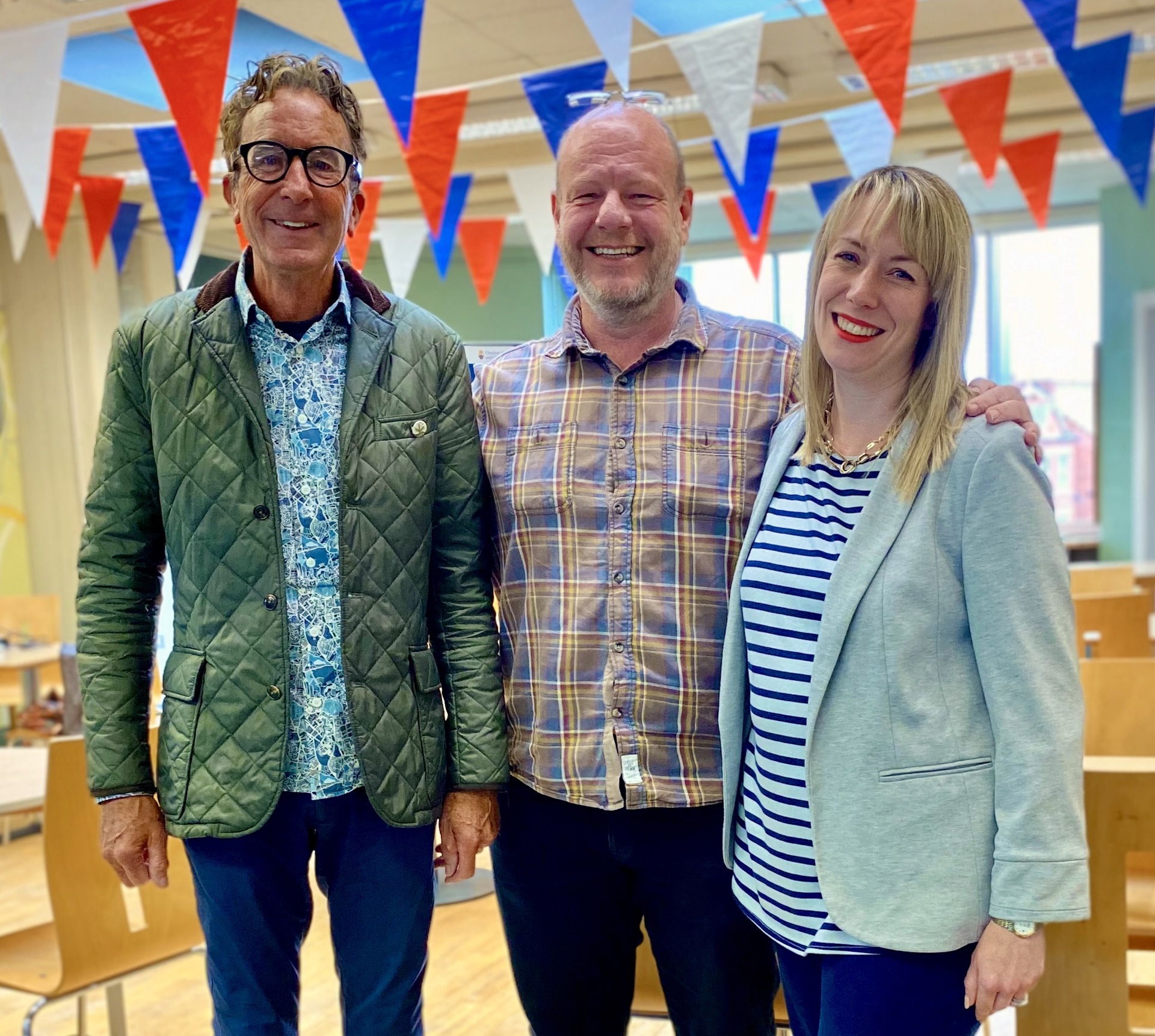 two white men and a white women standing smiling looking at the camera in a room with red blue and white bunting two white men and a white women standing smiling looking at the camera in a room with red blue and white bunting