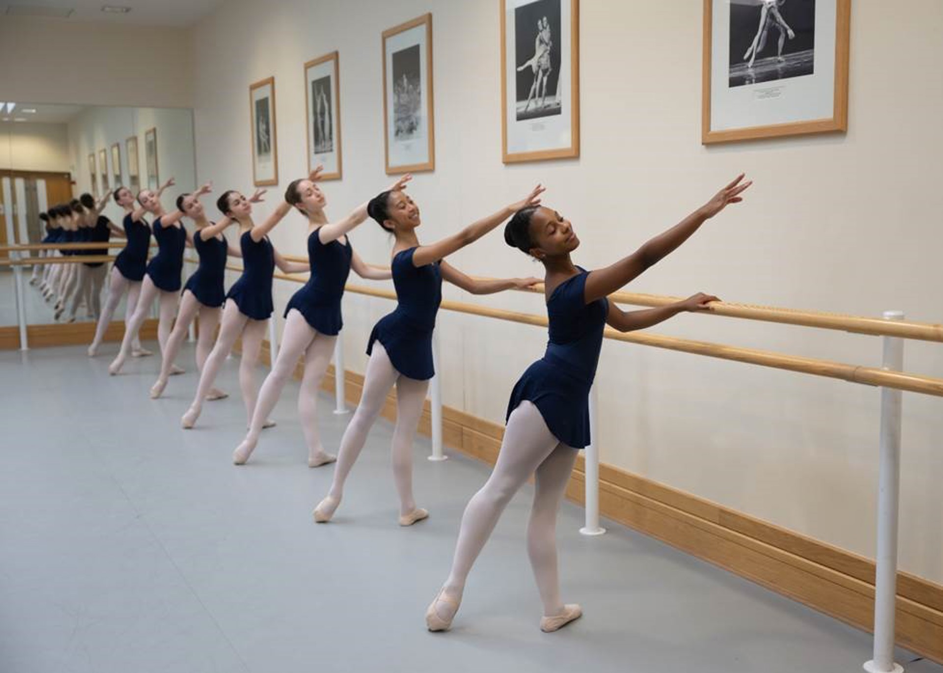 severn female young ballet dancers holding on to a ballet bar with one arm pointed to the top left of the image and the bottom left foot pointed away. Wearing blue leotards and pink tights. severn female young ballet dancers holding on to a ballet bar with one arm pointed to the top left of the image and the bottom left foot pointed away. Wearing blue leotards and pink tights.