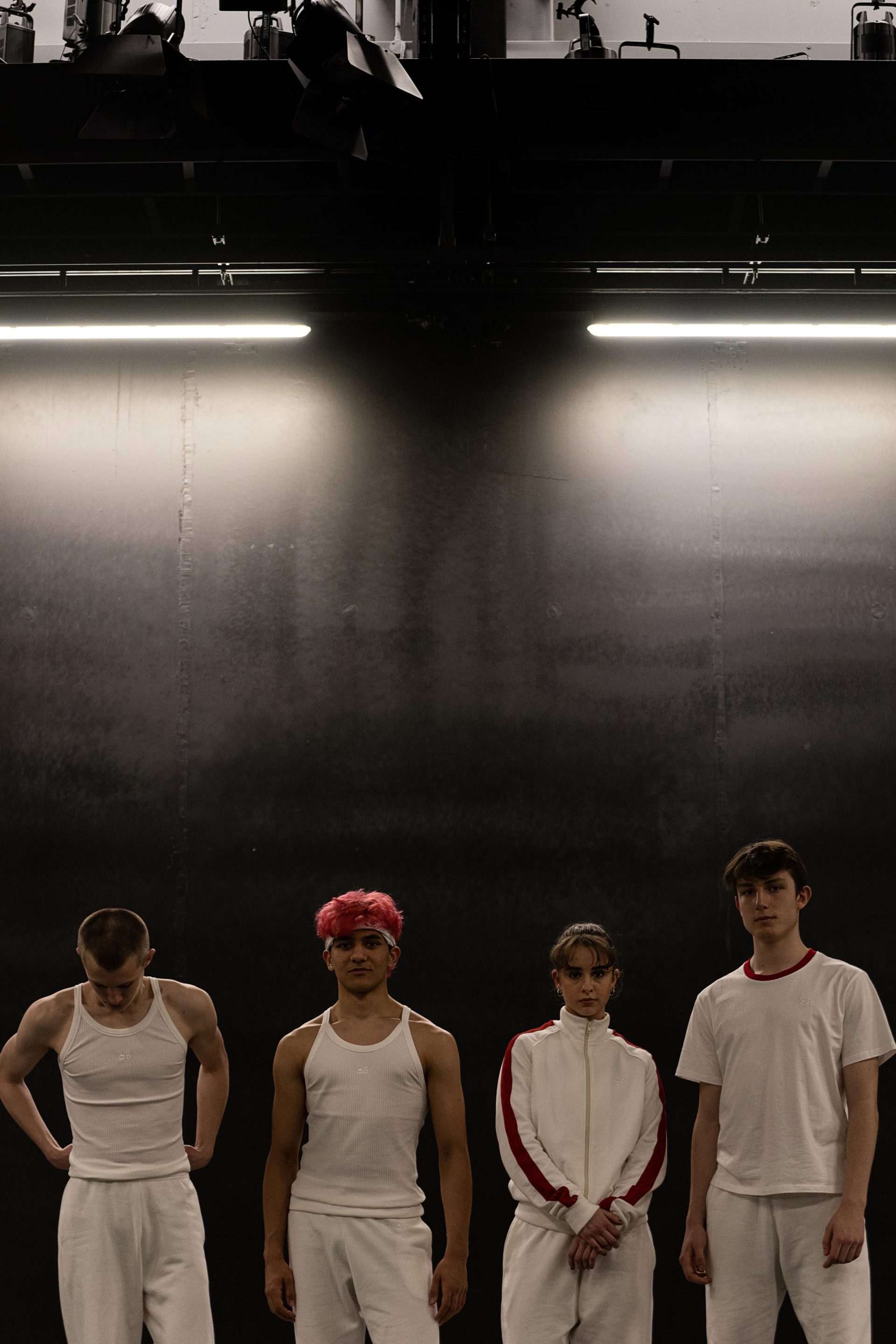 four young dancers wearing white tracksuits looking at the camera with dark walls behind them four young dancers wearing white tracksuits looking at the camera with dark walls behind them
