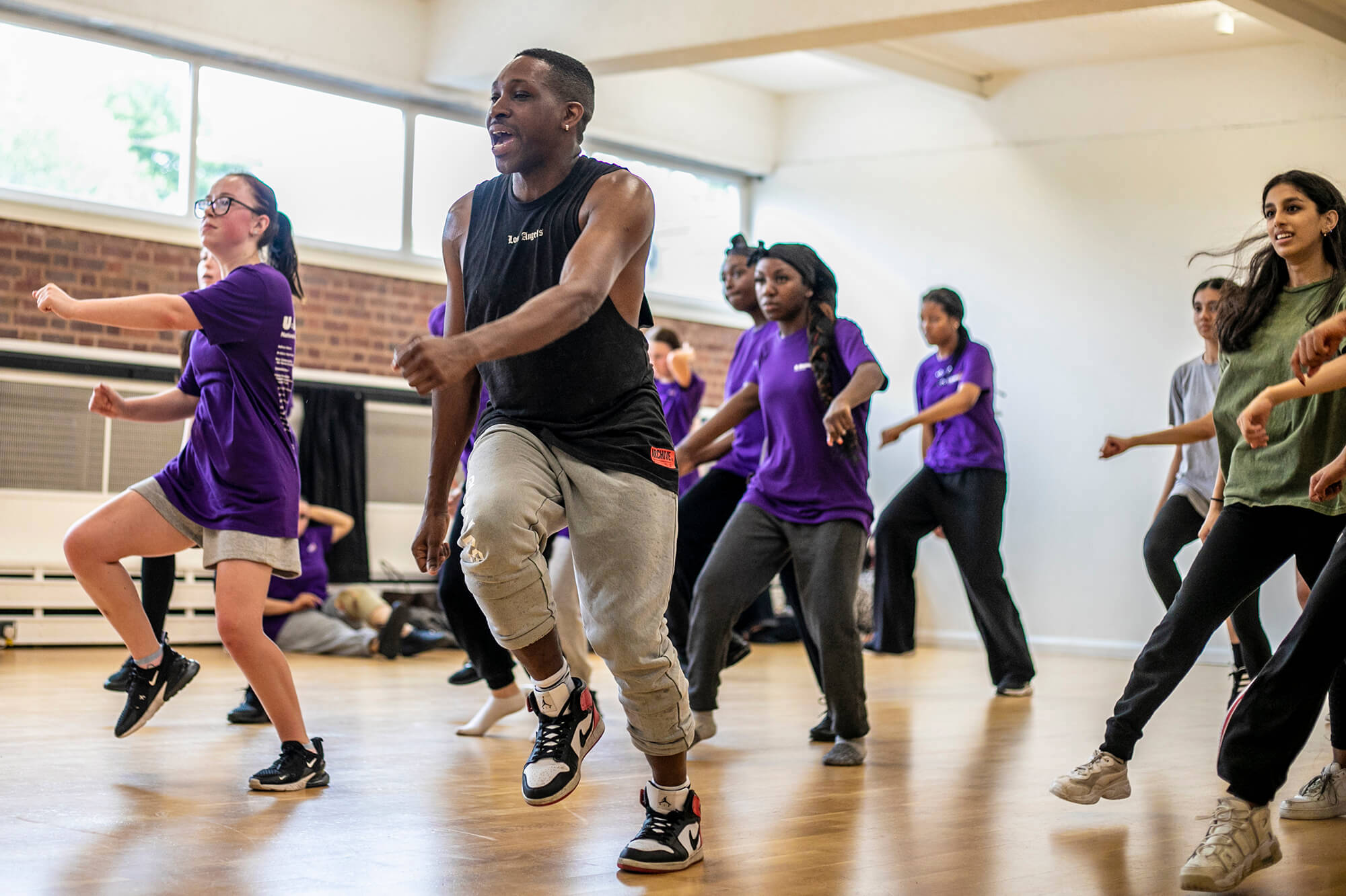 black male dancer teaching a group of young people to dance. all in a running man position wearing athletic clothing in a dance studio. black male dancer teaching a group of young people to dance. all in a running man position wearing athletic clothing in a dance studio.