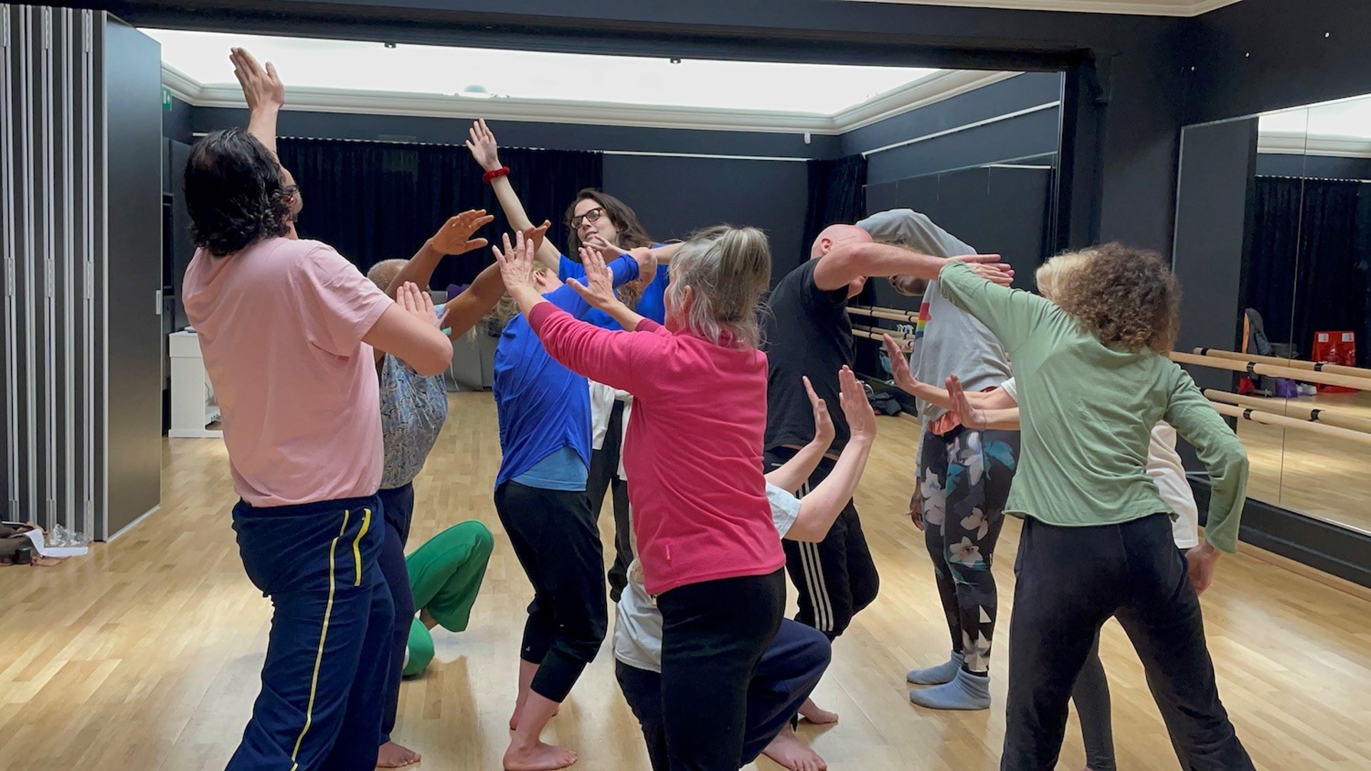 group of adults in colourful clothes in a dance studio moving around each other 