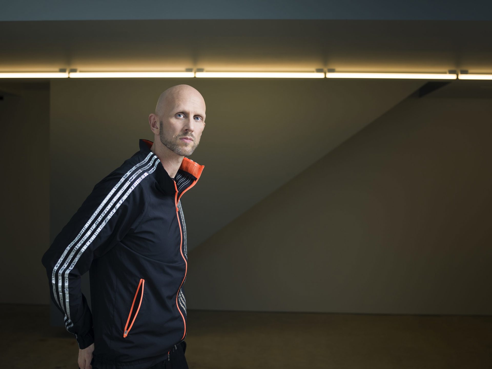 headshot of Wayne Mcgregor. White bald male with stubble standing to the left of image wearing a blue tracksuit zip up headshot of Wayne Mcgregor. White bald male with stubble standing to the left of image wearing a blue tracksuit zip up