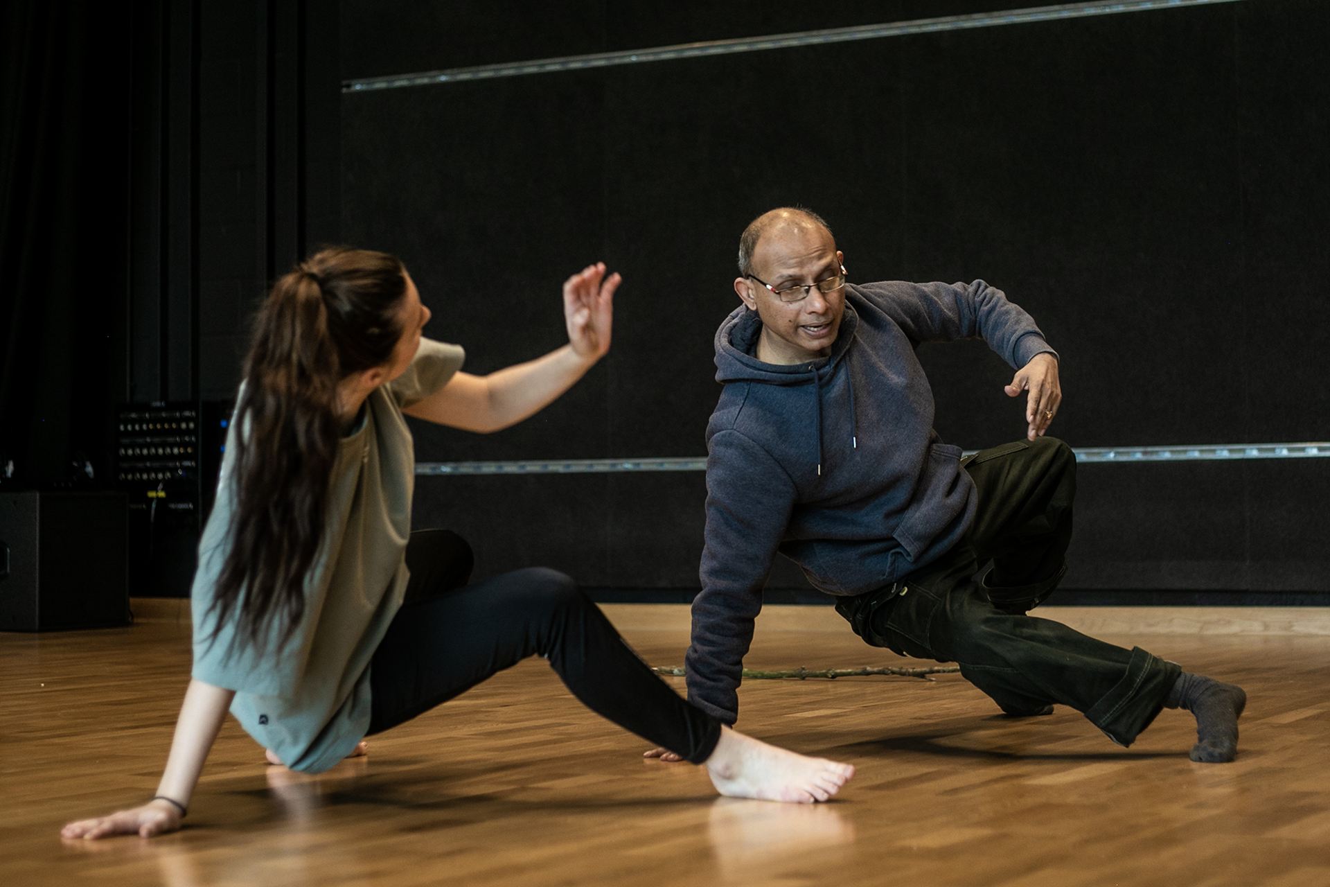 older male global majority dancer teaching white young female dancer. Both on the floor leaning on one hand. older male global majority dancer teaching white young female dancer. Both on the floor leaning on one hand.