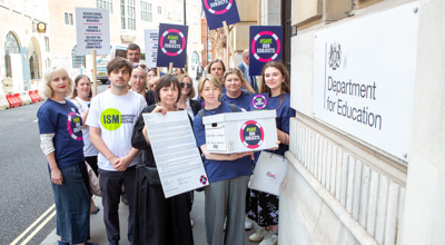 fourteen adults mixed genders standing in a group holding signs that say save our subjects outside the department of education