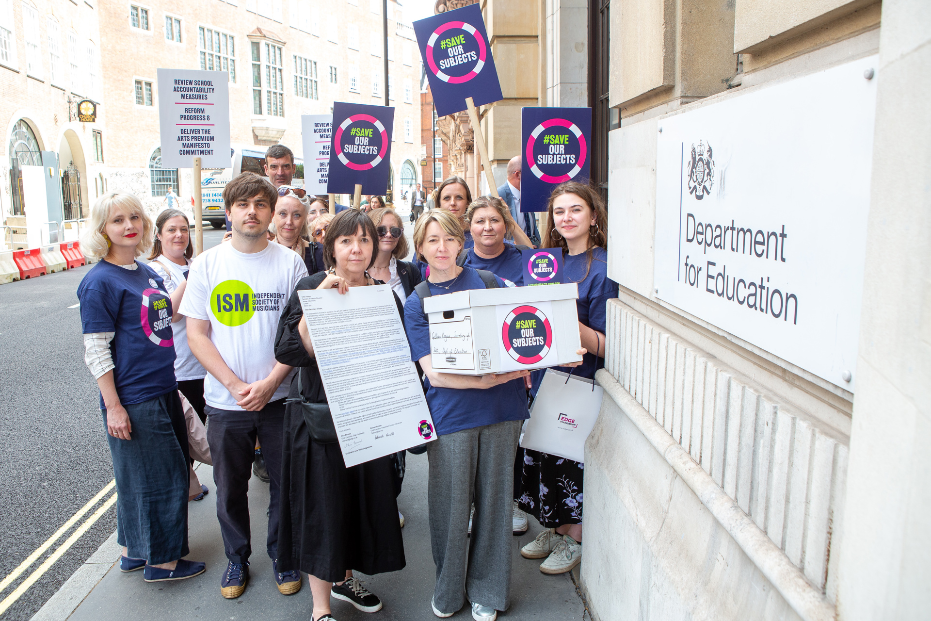 fourteen adults mixed genders standing in a group holding signs that say save our subjects outside the department of education fourteen adults mixed genders standing in a group holding signs that say save our subjects outside the department of education