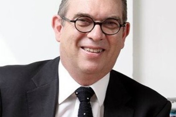 Headshot Anthony Bowne. White male smiling with circular glasses. Short grey hair, wearing a black suit, white shirt, and black tie.