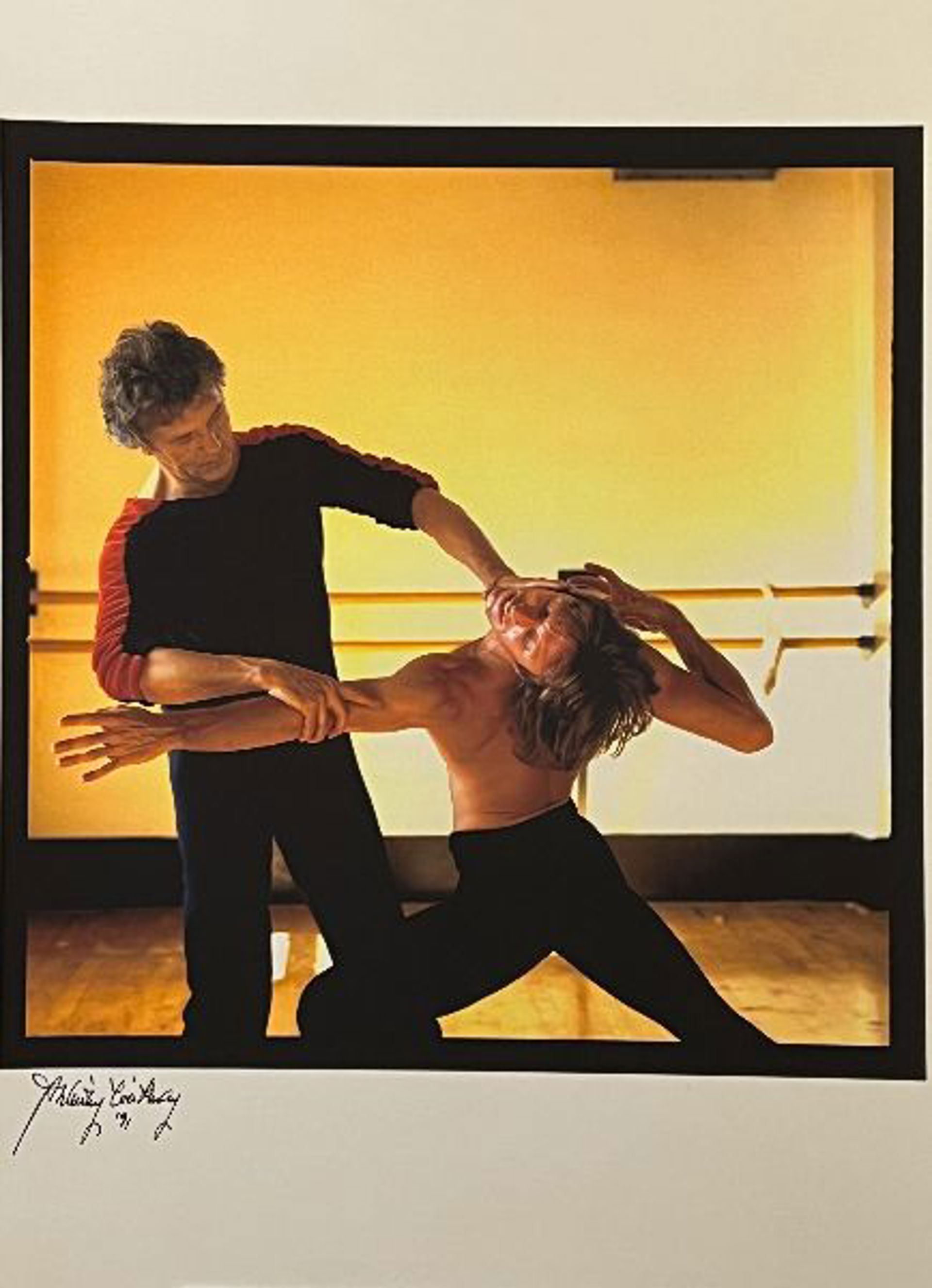 male dance teacher holding male dancers arm and head in movement in front of ballet bar in an orange lit dance studio male dance teacher holding male dancers arm and head in movement in front of ballet bar in an orange lit dance studio