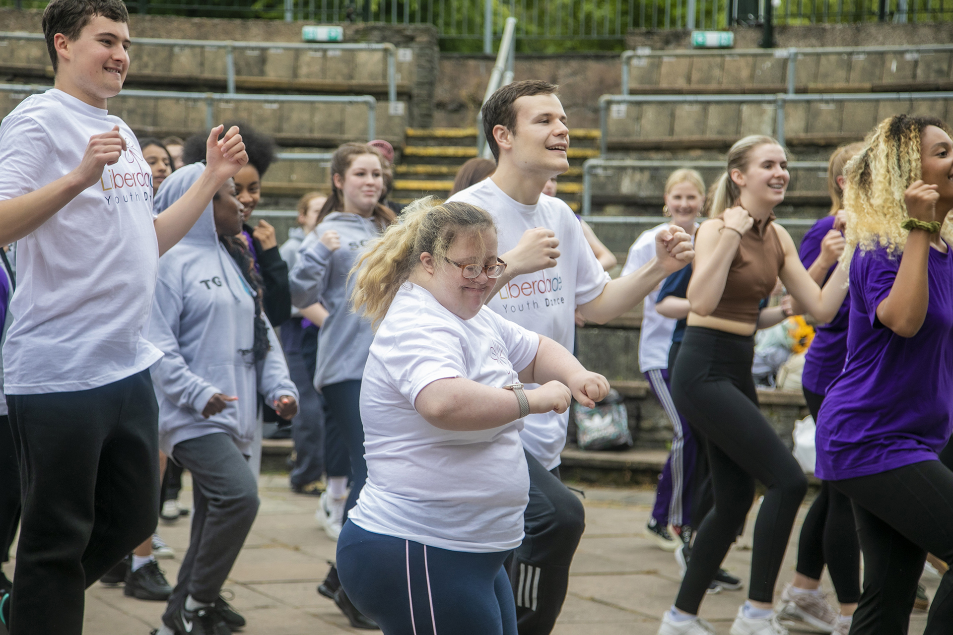 Young people dancing in an outdoor warm up, central dancer is a white female smiling. Wearing a mix of coloured outfits. Young people dancing in an outdoor warm up, central dancer is a white female smiling. Wearing a mix of coloured outfits.