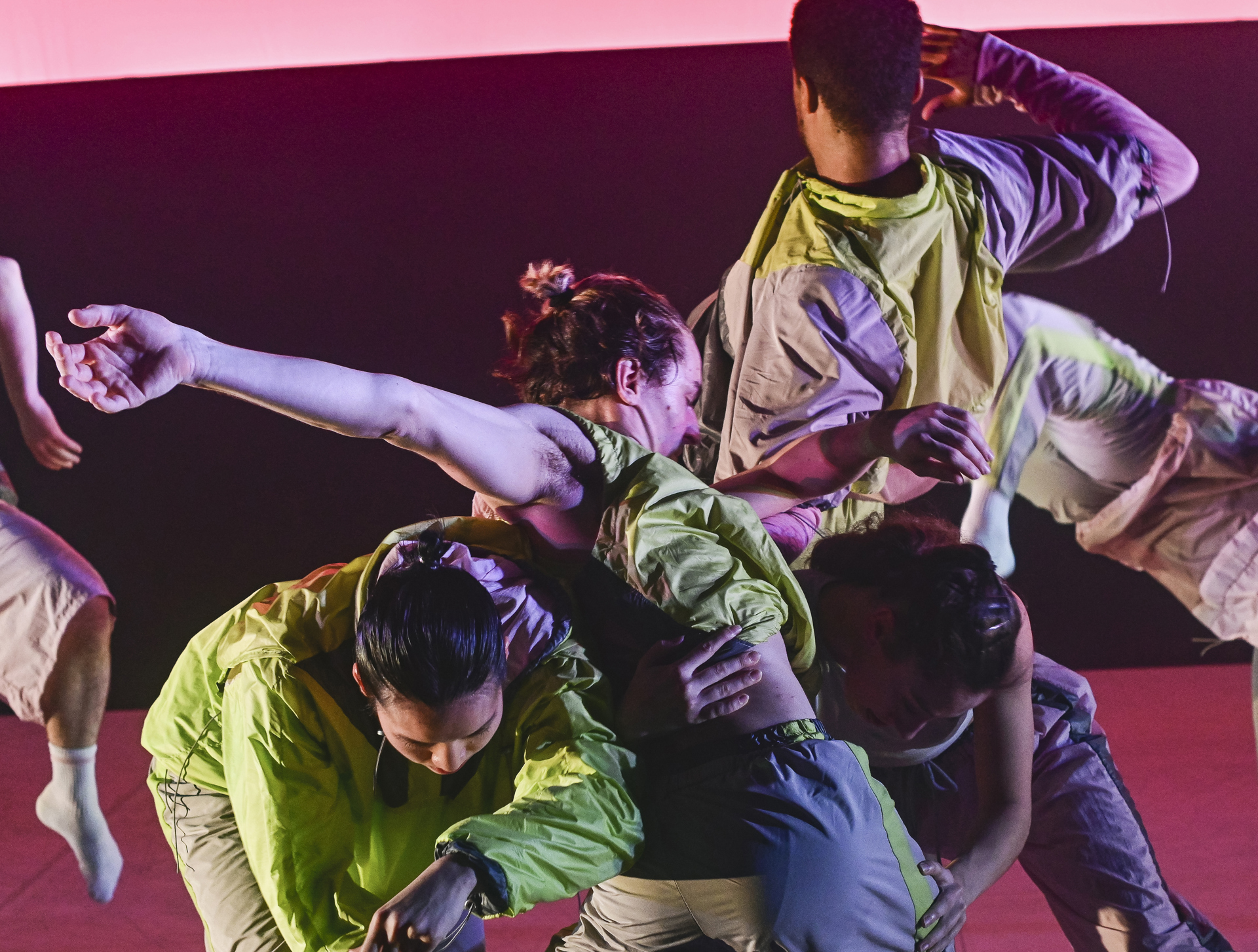 six dancers moving together in front of a striped pick and purple background