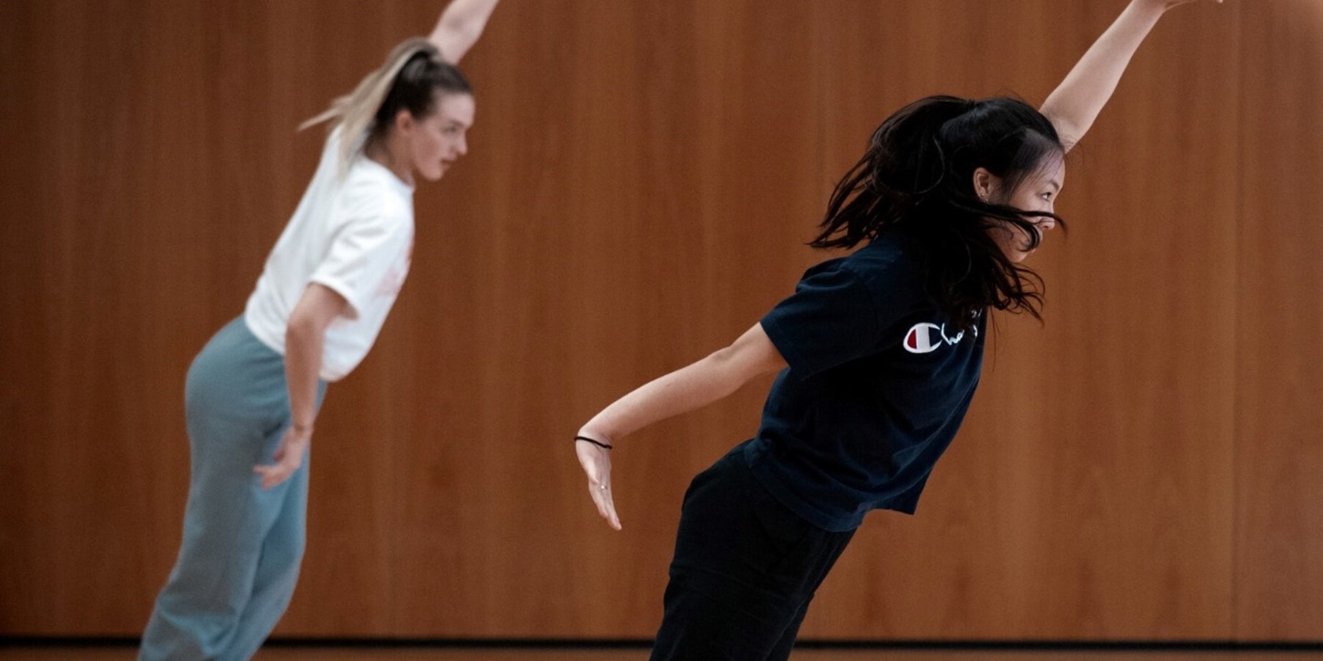 two young female dancers leaning diagonally with one arm up and other by their side. In front of wooden wall two young female dancers leaning diagonally with one arm up and other by their side. In front of wooden wall