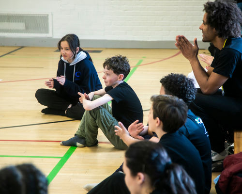 Dance students and their teachers applaud a performance in a sports hall