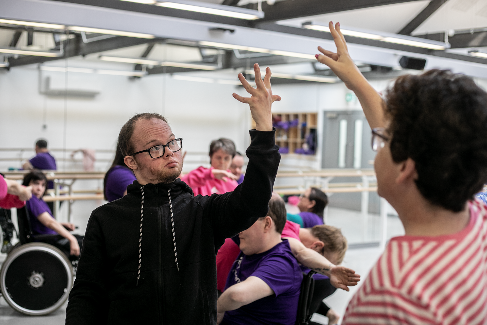 community dance group in the dance studio. Main focus on male downs syndrome dancer with hand stretched wide with other another dancer mirroring it.  community dance group in the dance studio. Main focus on male downs syndrome dancer with hand stretched wide with other another dancer mirroring it.