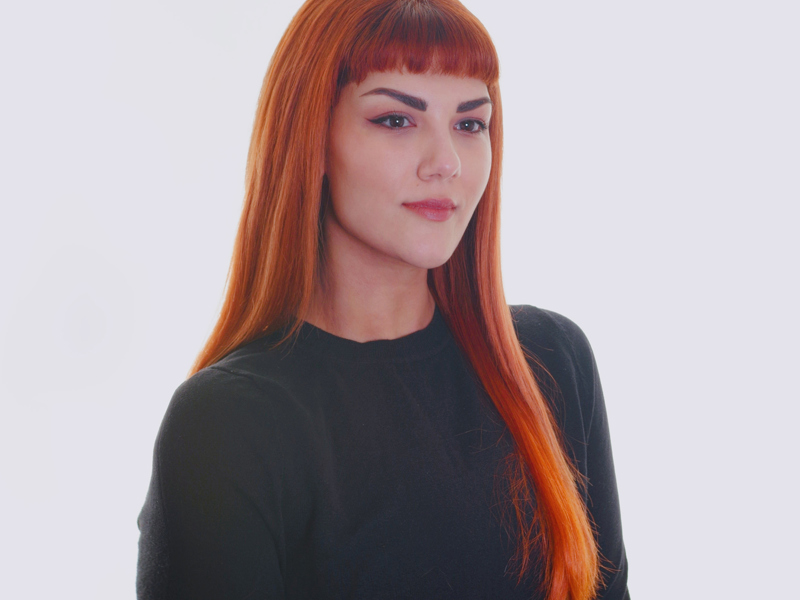 Headshot of Maria Nikolopoulou. Female with long red hair with fringe looking away from the camera. Wearing long sleve black top Headshot of Maria Nikolopoulou. Female with long red hair with fringe looking away from the camera. Wearing long sleve black top