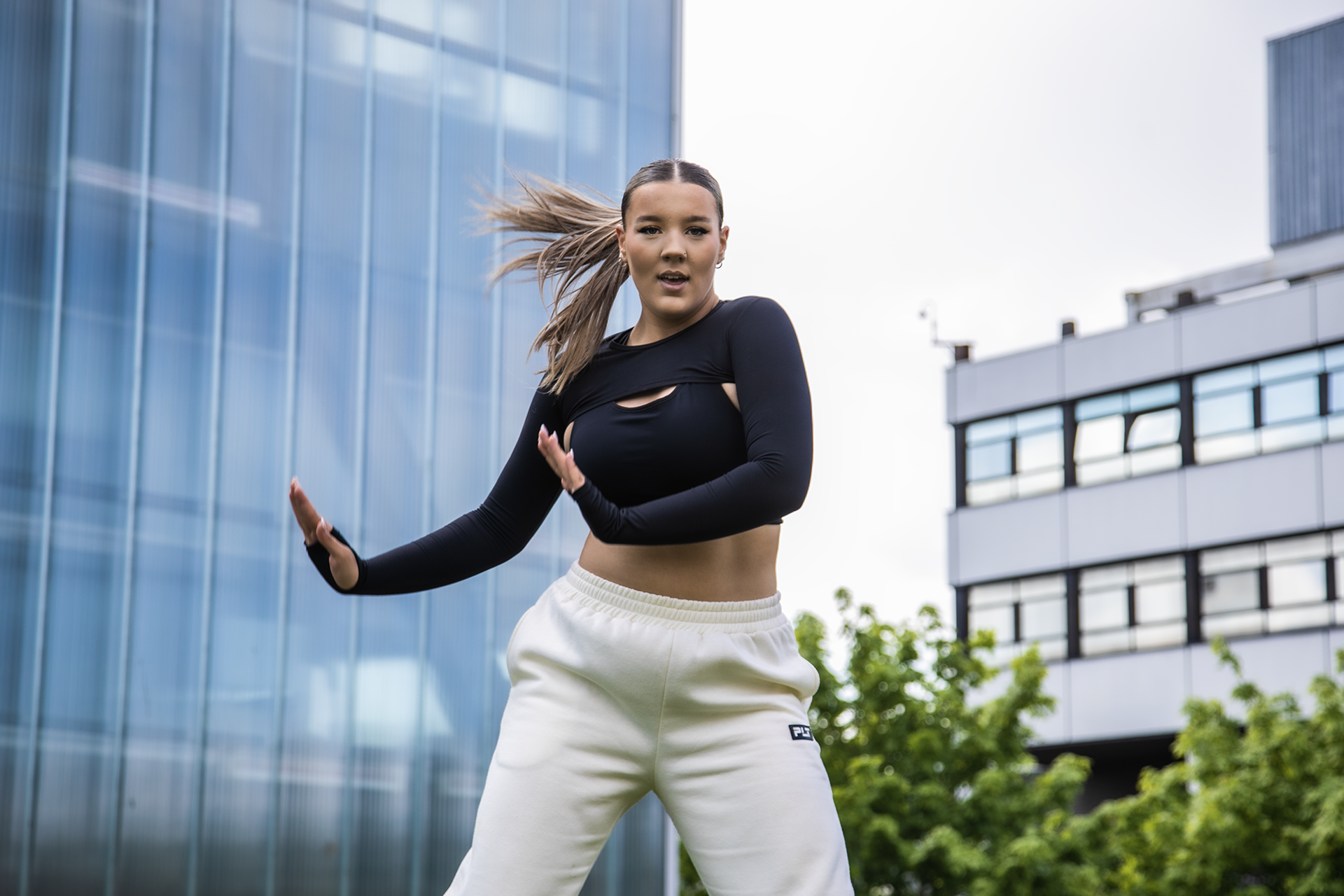 young female dancer with arms to the right side of her infront of Newcastle college building. Wearing black top, white joggers and ponytail swinging to the left young female dancer with arms to the right side of her infront of Newcastle college building. Wearing black top, white joggers and ponytail swinging to the left