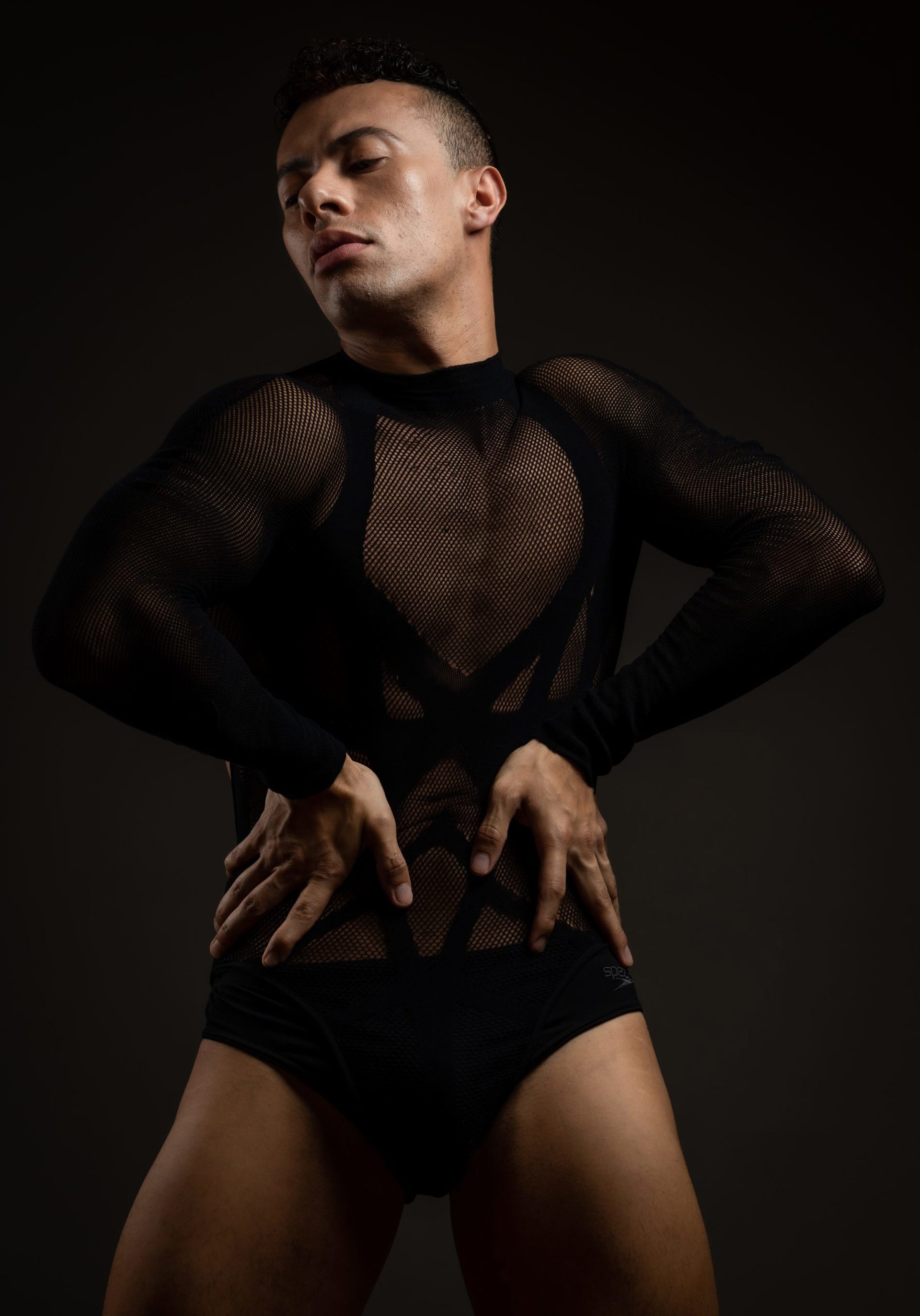 male dancer with hands on hips wearing fishnet leotard looking down male dancer with hands on hips wearing fishnet leotard looking down