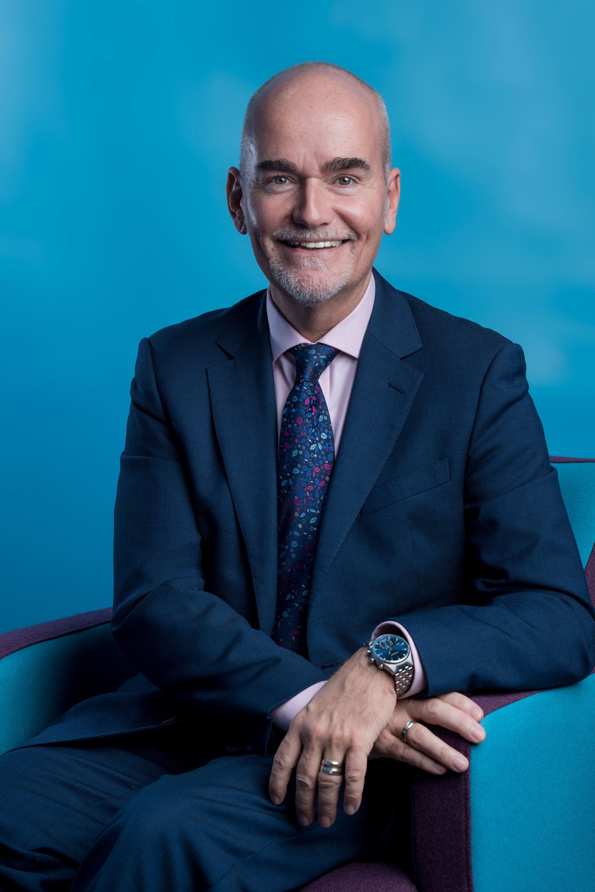 Headshot of David Blackburn. White man with shaved head smiling at the camera wearing and blue suit and tie Headshot of David Blackburn. White man with shaved head smiling at the camera wearing and blue suit and tie