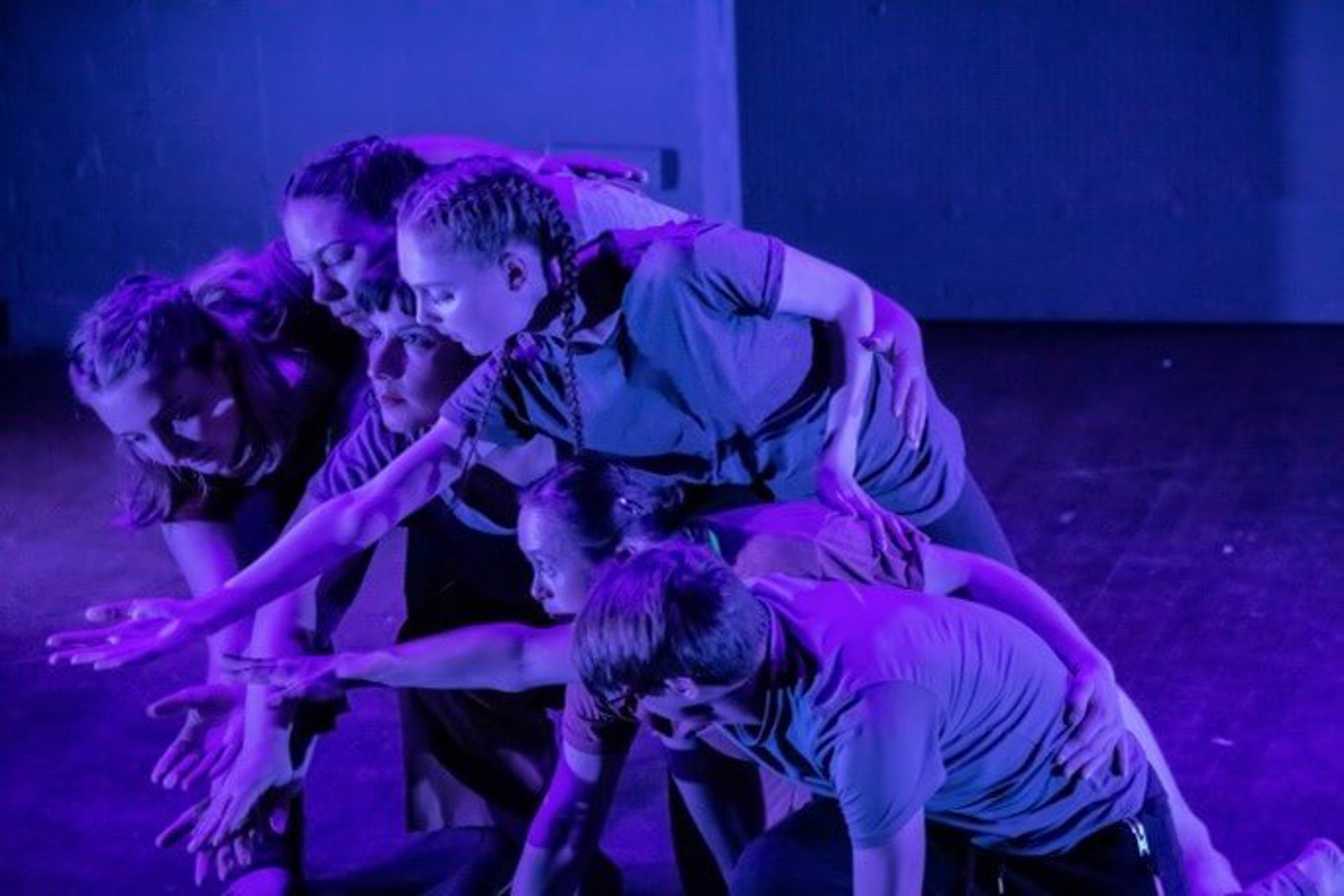 six young dancers all huddled together reaching for the same spot in the bottom left on the screen with blue lighting six young dancers all huddled together reaching for the same spot in the bottom left on the screen with blue lighting