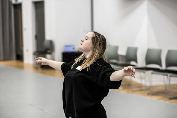 White blonde female down syndrome dancer with arms spread out head up wearing black in a dance studio 