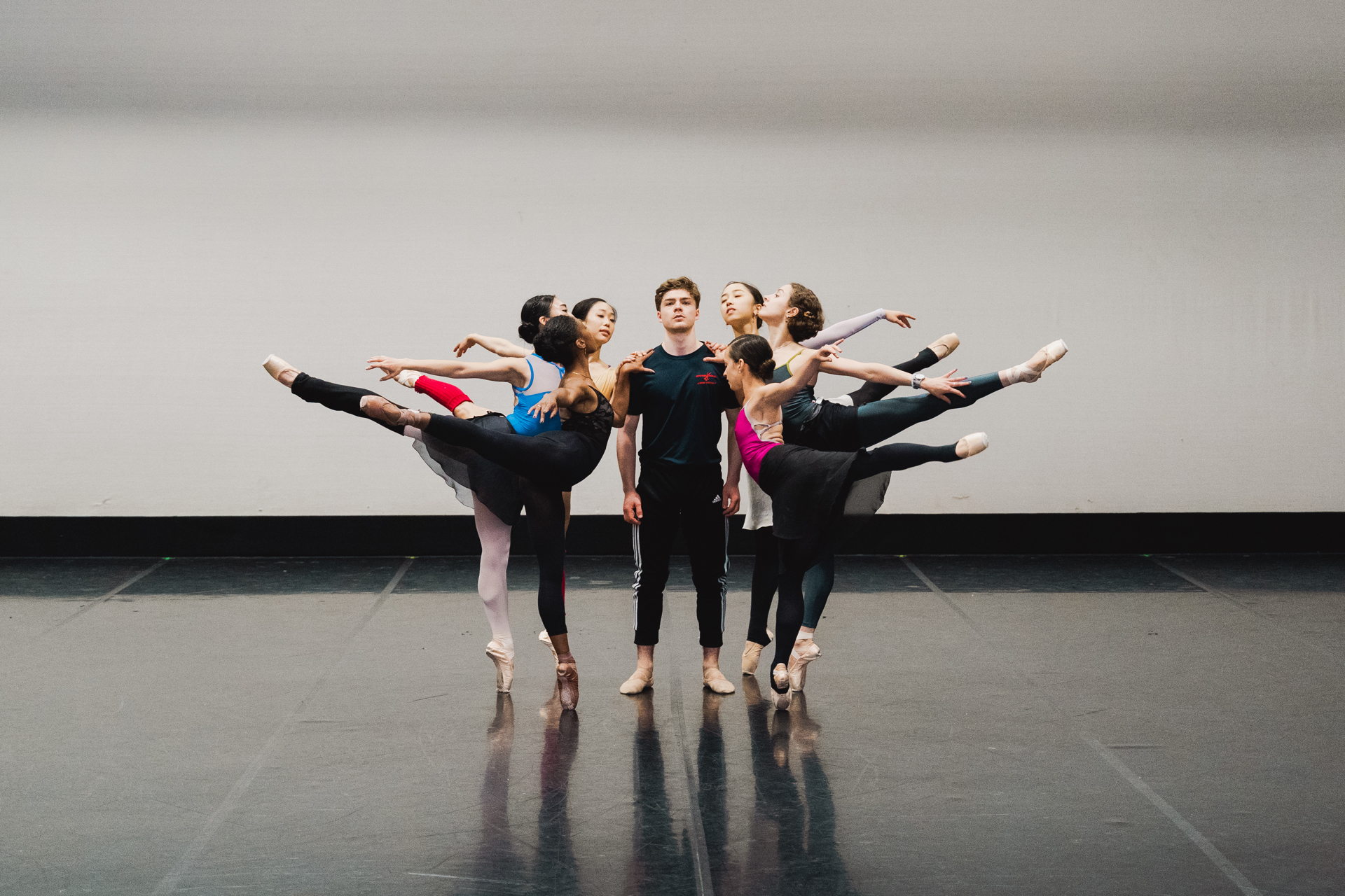 six females on point in an arabesque with leg high behind all holding onto centre male who is standing looking at the camera. In a dance studio six females on point in an arabesque with leg high behind all holding onto centre male who is standing looking at the camera. In a dance studio