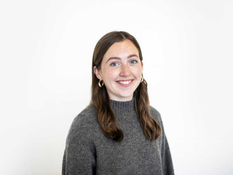Headshot of Chloe Sprackling white female with brown hair smiling at the camera. Wearing gold hoop earrings and high neck grey jumper Headshot of Chloe Sprackling white female with brown hair smiling at the camera. Wearing gold hoop earrings and high neck grey jumper