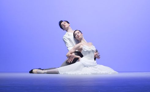 male and female ballet dancers lunged on the floor looking up and to the left on blue background
