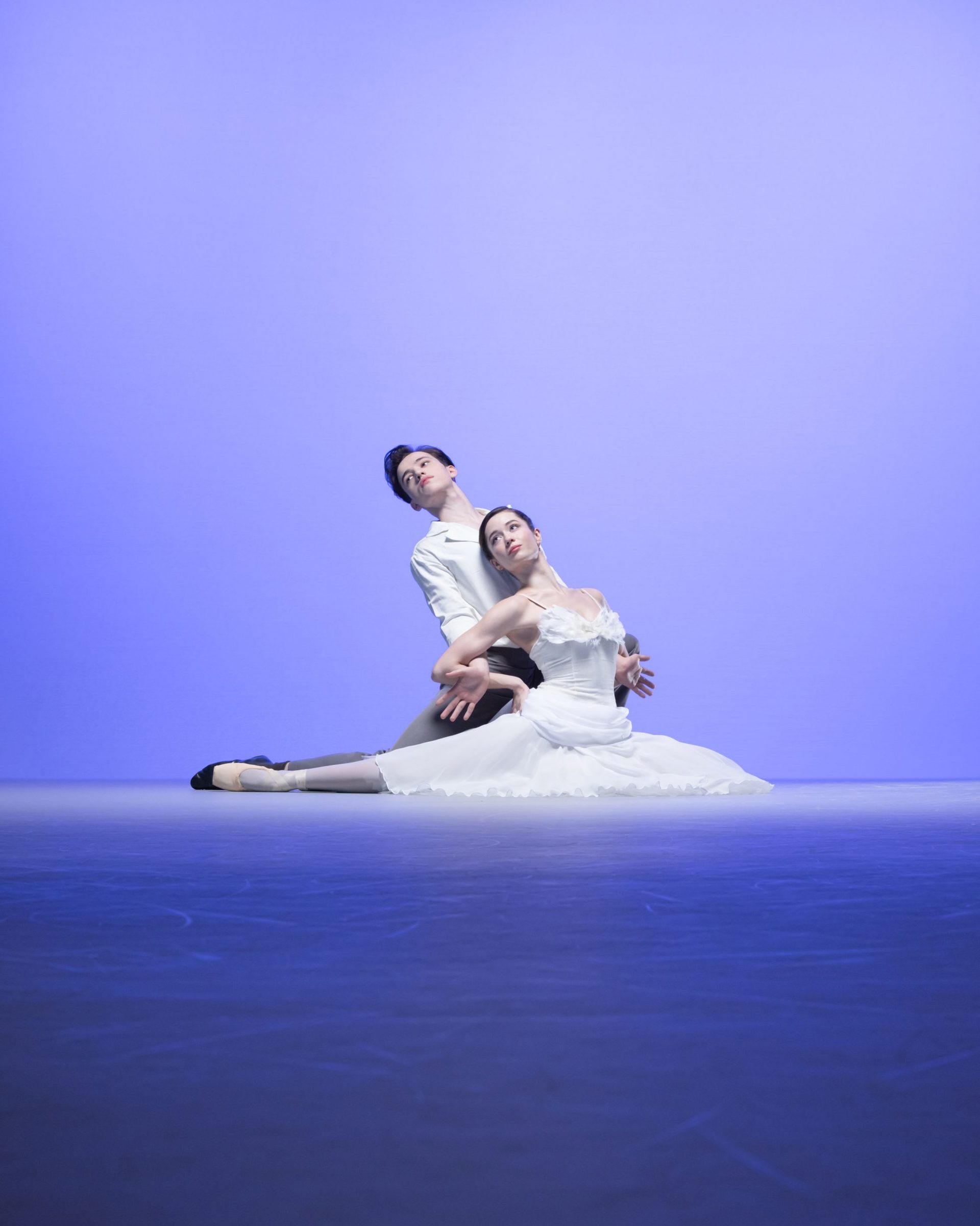 male and female ballet dancers lunged on the floor looking up and to the left on blue background