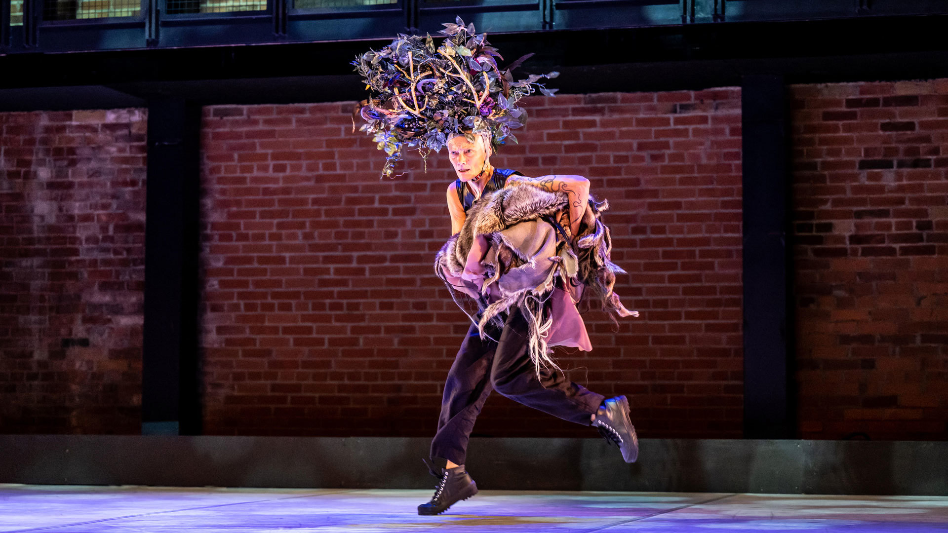 white female dancer running across the stage with large tree head piece carrying lots of clothes with brick background white female dancer running across the stage with large tree head piece carrying lots of clothes with brick background
