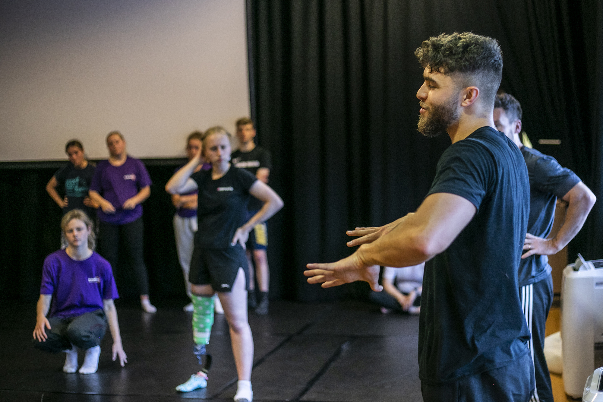 white male dancer guestering to dance students in a blacked out dance studio